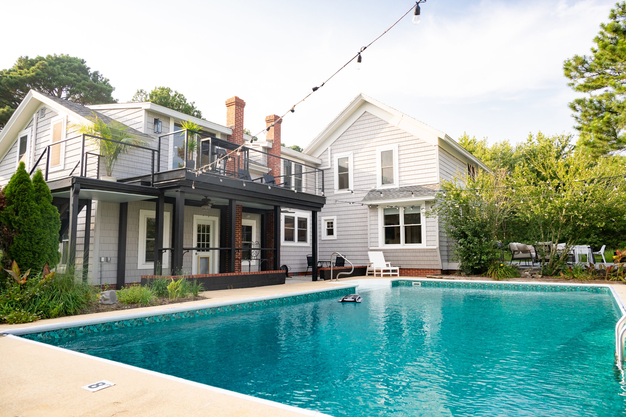 The in-ground pool and rear of the farmhouse under string lights