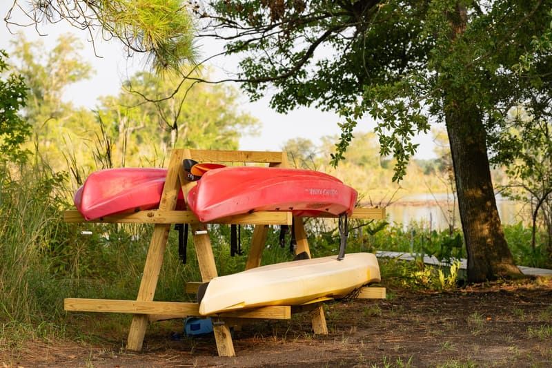 Guest kayaks on a rack under the trees by the water